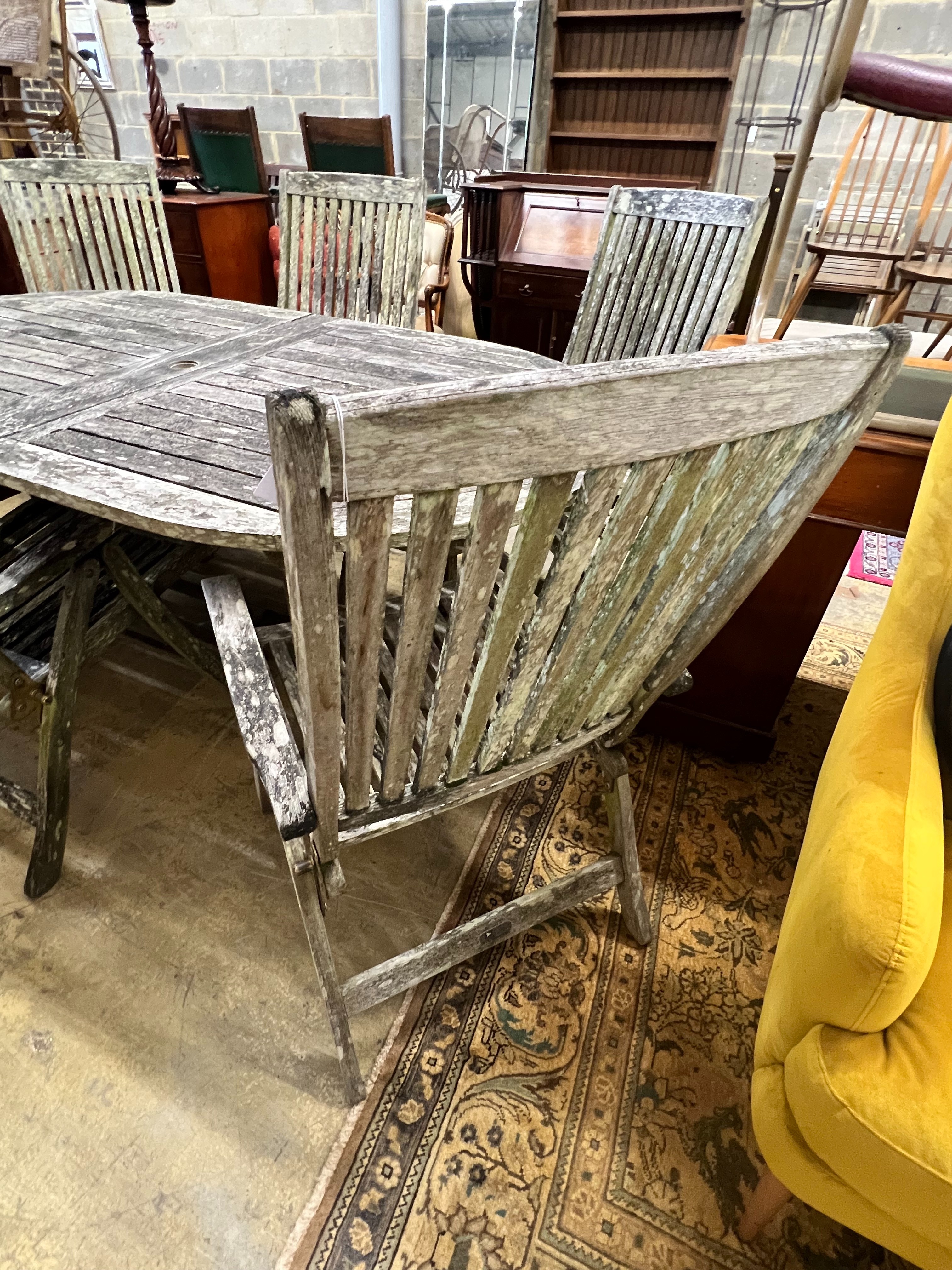 A weathered teak oval extending garden table, extended 250cm width 109cm height 73cm, and six folding garden elbow chairs